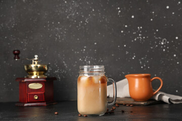 Mason jar of iced latte and coffee beans on black background