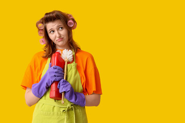 Thoughtful young woman with hair curlers holding toilet brush and detergent on yellow background