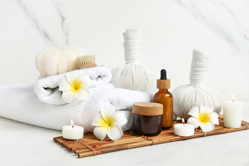 Set of spa supplies with different cosmetic products, herbal bags, plumeria flowers and burning candles on white background