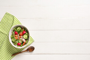 Bowl of fresh vegetable salad with radish and cucumber on white wooden background