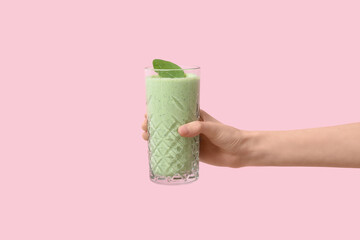 Female hand with glass of fresh spinach smoothie on pink background