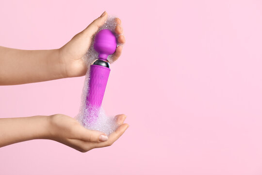 Woman washing purple vibrator on pink background, closeup