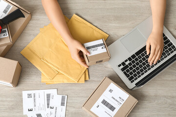 Female postal worker with parcel using laptop on table, top view