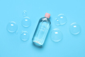 Bottle of micellar water and soap bubbles on blue background