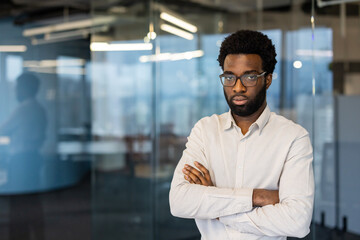 Fototapeta premium An African American man stands confidently with his arms crossed in a modern office space, exuding professionalism and determination.