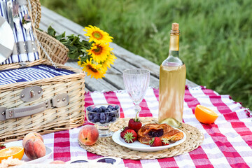 Wicker basket with sunflowers, tasty food and bottle of wine for romantic picnic in park