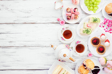 Afternoon tea side border against a white wood background. Vintage tea set, finger sandwiches,...