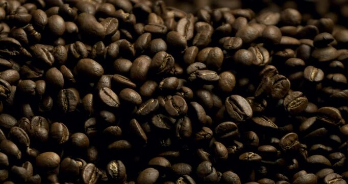 Super slow motion macro of fresh flavorful aromatic roasted coffee beans in rustic bag are falling on wooden table in coffee production shop at 1000 fps.