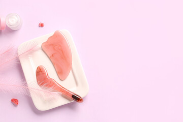 Plate with facial massage tools and jar of cosmetic product on pink background