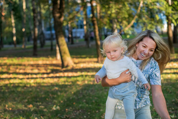 Fototapeta premium A happy mother plays with her son outside in the park on a sunny summer day. Mom and baby have fun together. The concept of family, happiness and love.