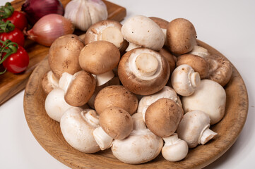 White and brown champignons mushrooms fresh uncooked on wooden plate copy space on white background