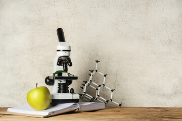 Modern microscope with apple, book and molecular model on wooden table against white grunge...