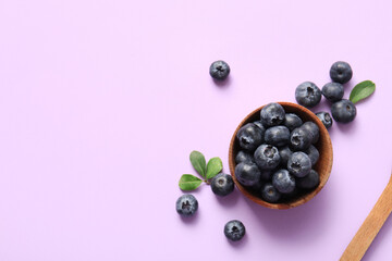Wooden bowl with fresh ripe blueberry on lilac background