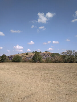 Dry grass field leading to rocky hill Wild Sarka under blue sky with clouds