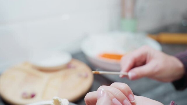 Close-up hand view of person holding creamy butter on fingertip, preparing to drop it into pot of smooth brown pap in bright kitchen