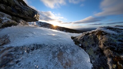 Fototapeta premium Frozen ice and snow cover rocky mountain terrain during a bright golden sunrise under a blue sky.