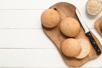 Board of fresh buns with sesame seeds on white wooden background
