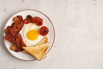 Plate with fried egg, bacon, toasts and dried tomatoes on white background. Top view