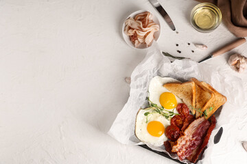 Fried bacon and eggs on parchment paper on white table. Top view