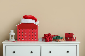Christmas advent calendar with gift boxes and decorations on commode near beige wall at home