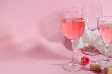 Glasses of wine, rose and cloth on pink background