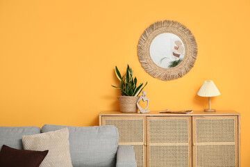 Cozy sofa, chest of drawers and mirror on yellow wall in living room
