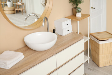 Sink bowl, chest of drawers and laundry basket near beige wall in bathroom