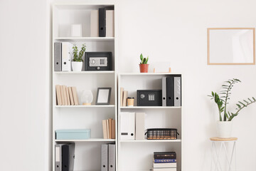 Modern safes, houseplants and office folders on shelving unit near white wall