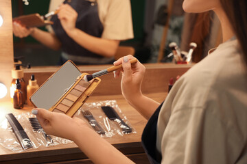 Female makeup artist with brush and eyeshadows in dressing room at night, closeup