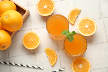 Glasses of fresh orange juice with mint and fruits on white tile background