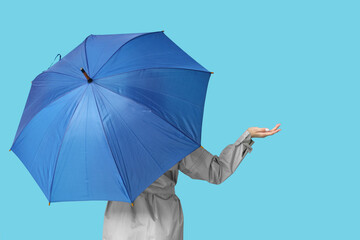 Young woman with umbrella on  blue background, back view