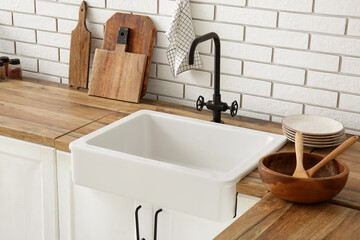 White ceramic sink and boards on wooden counter near white brick wall in kitchen