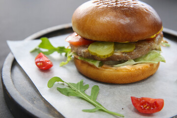 Hamburger in a restaurant on a tray and parchment paper, there are also arugula and tomatoes on the paper