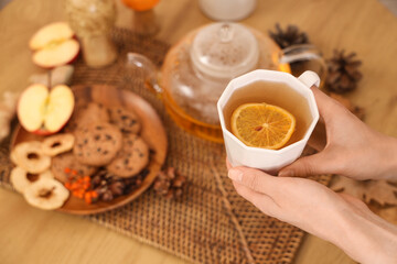 Female hands with cup of green tea near plate with food and autumn decor on table in room. Closeup