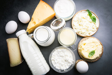 Fresh dairy products, milk, cottage cheese, eggs, yogurt, sour cream and butter on black background, top view