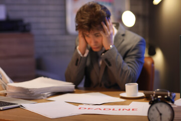 Naklejka premium Paper with word DEADLINE on table against stressed businessman in office at night, closeup