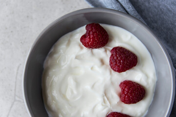 Gray bowl and natural yogurt with berries on the stone marble table.
