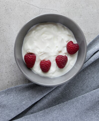 Gray bowl and natural yogurt with berries on the stone marble table.