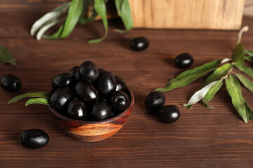 Bowl with tasty black olives and leaves on wooden background