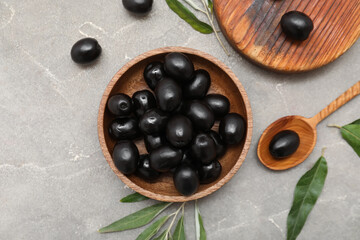 Wooden bowl with tasty black olives and leaves on grey background
