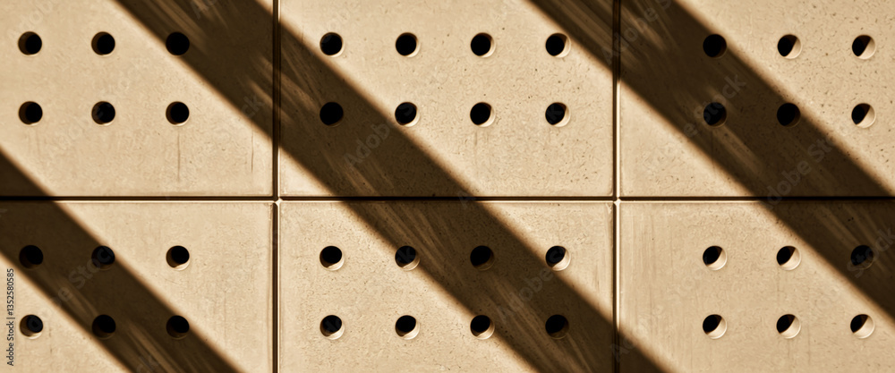 Aufkleber beige square panels with circular perforations, angled sunlight casting diagonal shadows, creating a