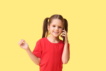 Fototapeta premium Happy little girl talking by phone on yellow background