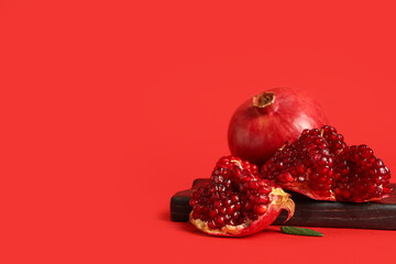 Wooden board with fresh ripe pomegranates on red background
