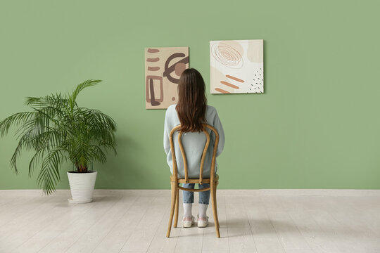 Young woman on chair looking at paintings in art gallery, back view
