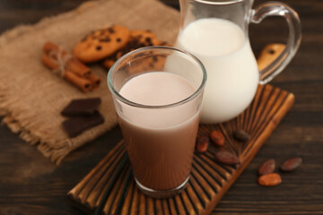 Glass of sweet chocolate milk with cocoa beans and tasty cookies on wooden background