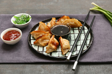 Plate of fried Japanese gyoza with bowls of sauces and seaweed salad on black background
