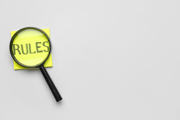 Sticky note with word RULES and magnifier on light background