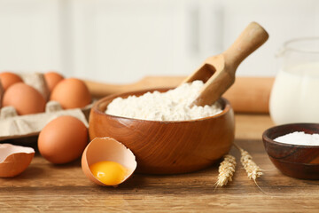 Bowl of flour with scoop, eggs, wheat spikelets and salt for preparing dough on kitchen counter