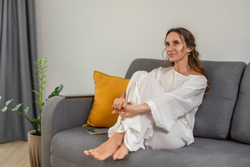 Woman Relaxation Home: Peaceful indoor scene showing a woman relaxing on a gray couch at home,...