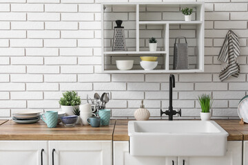 Wooden kitchen counter with sink, clean dishes and shelving unit hanging on light brick wall